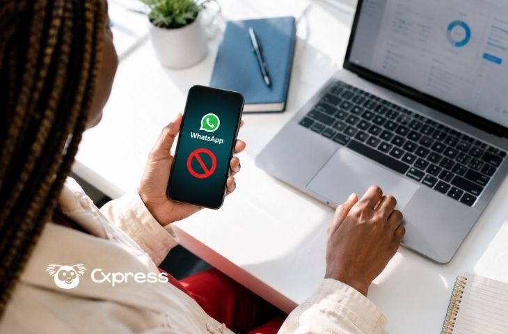Mulher segurando o celular com o WhatsApp bloqueado na tela enquanto mexe no notebook com um dashboard aberto